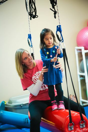 A girl stands on a swing and is held by a therapist