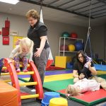 Two therapists assist children on equipment