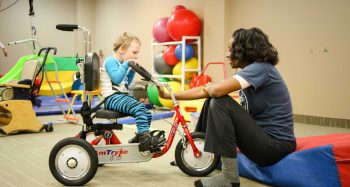 A therapist assists a boy on a trike